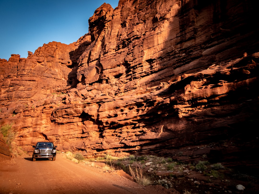 A truck driving down a dirt desert road with dust trailing behind it
